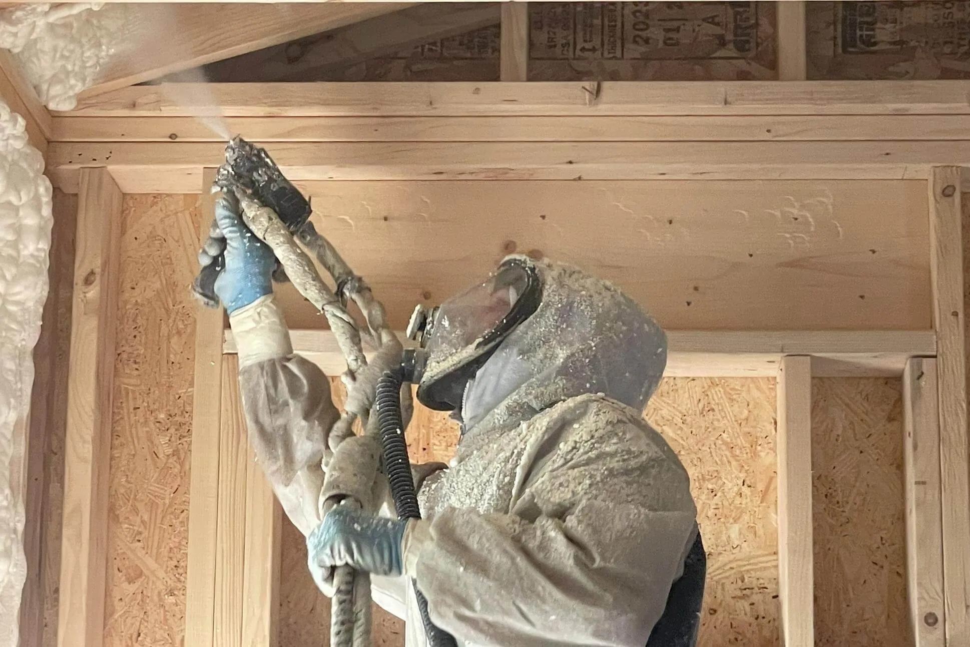Installer spraying foam overhead with protective sheeting in place